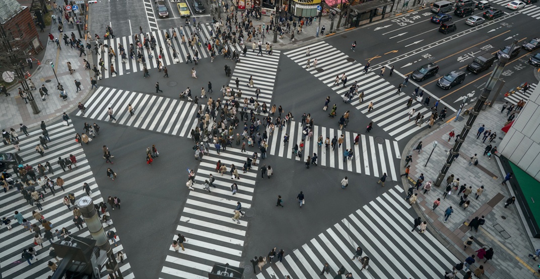 Birds eye view of a 6 way pedestrian crossing in Japan. There are lots of people walking in all sorts of confused directions.