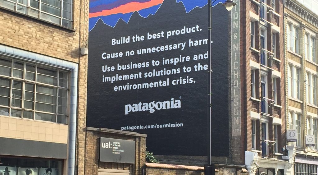 A streetscape looking up at a Patagonia billboard that says'Build the best product. Cause no unnecessary harm.